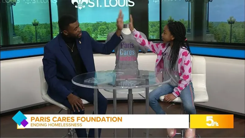 Paris high-fiving a TV host in a St. Louis studio next to a Paris Cares Foundation shirt